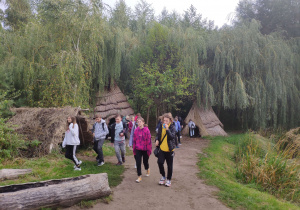 Grupa uczniów spacerująca w Muzeum Archeologicznym w Biskupinie. Za plecami widać drewniane szałasy.